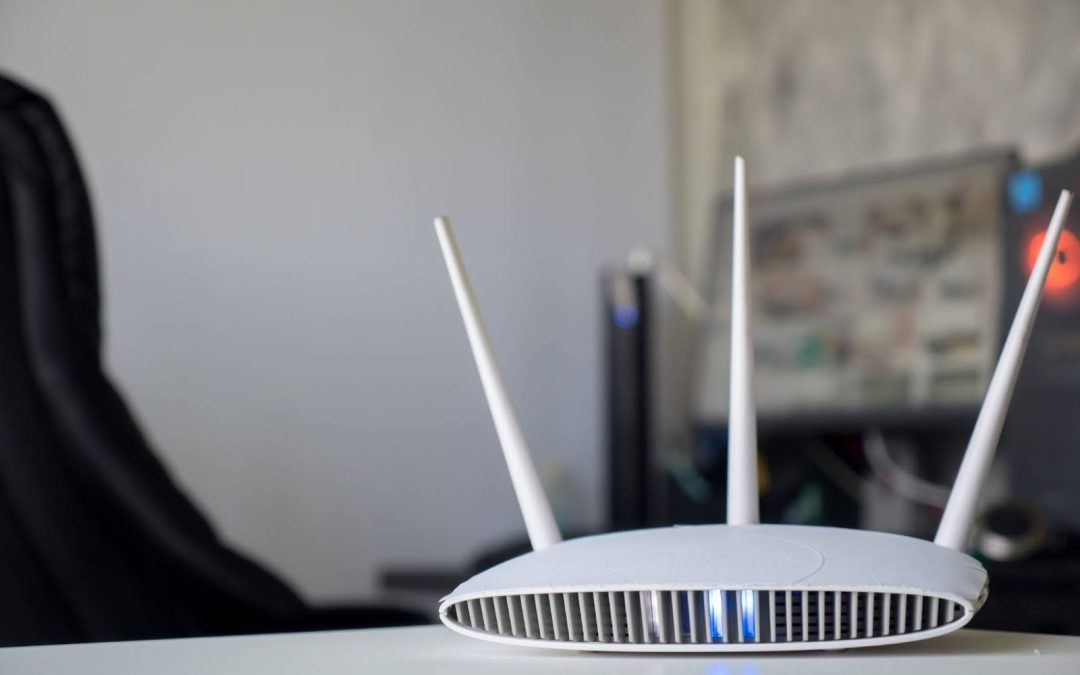 A white Wi-Fi router with blue lights on sits on a desk in a home office