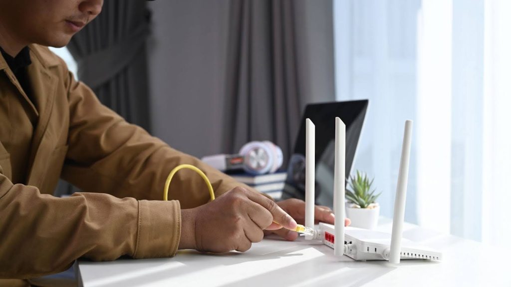 Close-up of a person inserting a yellow Ethernet cable into the rear LAN port of a white wireless router.
