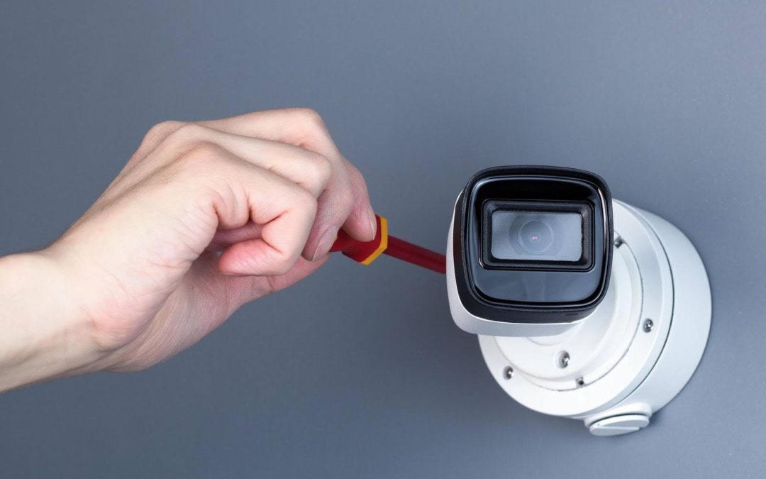 A technician's hand using a screwdriver to repair a mounted security camera to resolve why CCTV camera not working